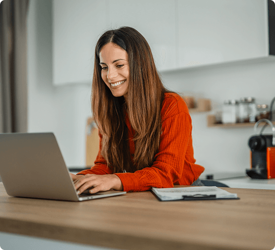 A smiling woman works from a laptop in a kitchen